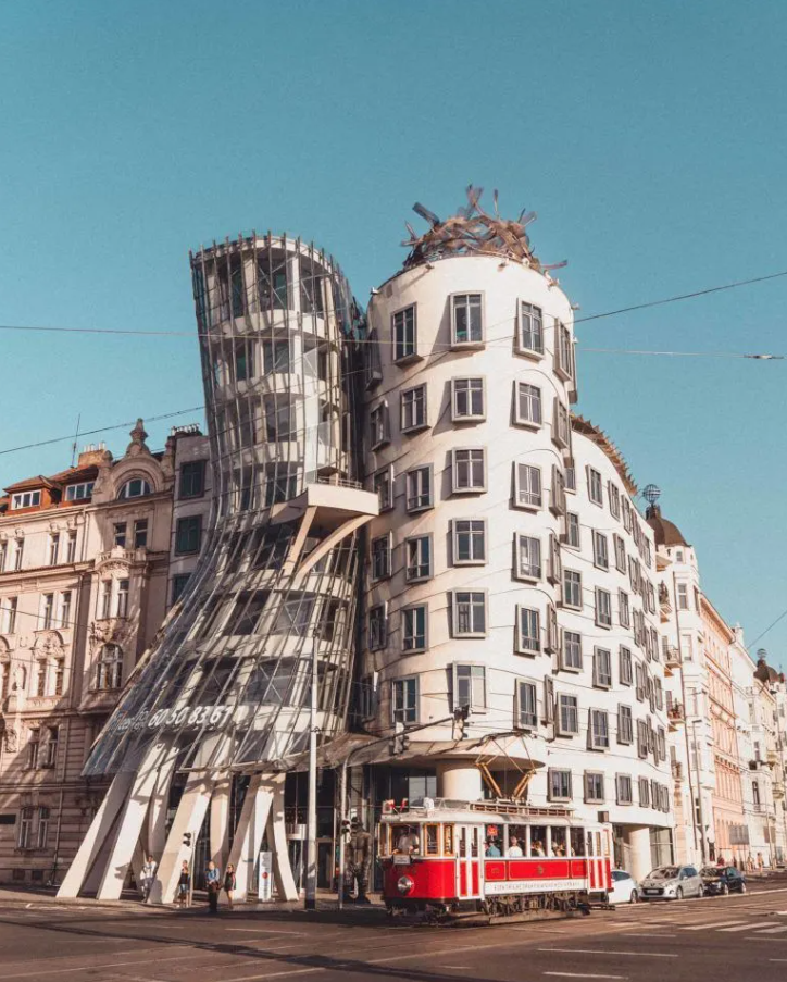 Photo of Prague's Dancing House, a unique building with flowing lines and curved shapes. The building is a mix of glass and concrete, and has a playful and whimsical design. The photo captures the building's exterior, with the blue sky and fluffy clouds in the background #Prague #CzechRepublic #DancingHouse #Architecture #Travel #UniqueDesign #Whimsical #GlassAndConcrete #Cityscape #Wanderlust